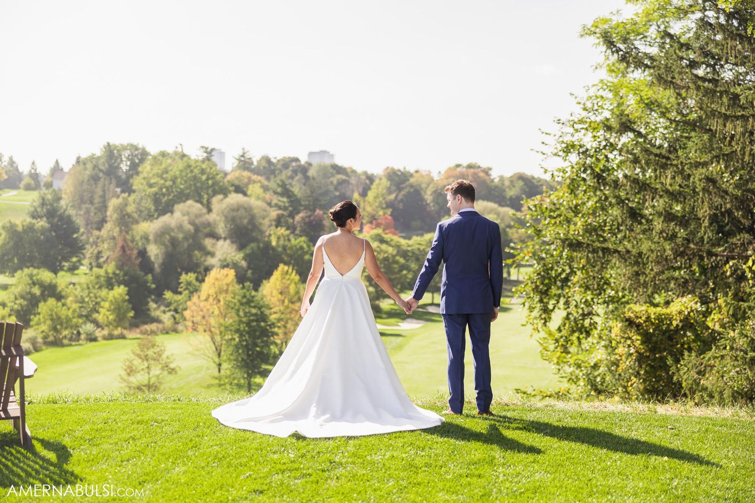 Newlyweds stand together on a scenic hillside overlooking green landscapes.