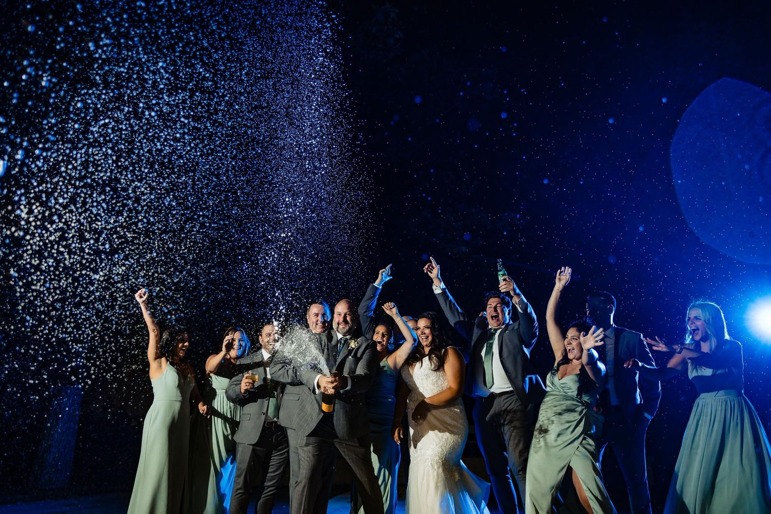 Wedding party celebrating under falling sparklers against a dark blue night sky.