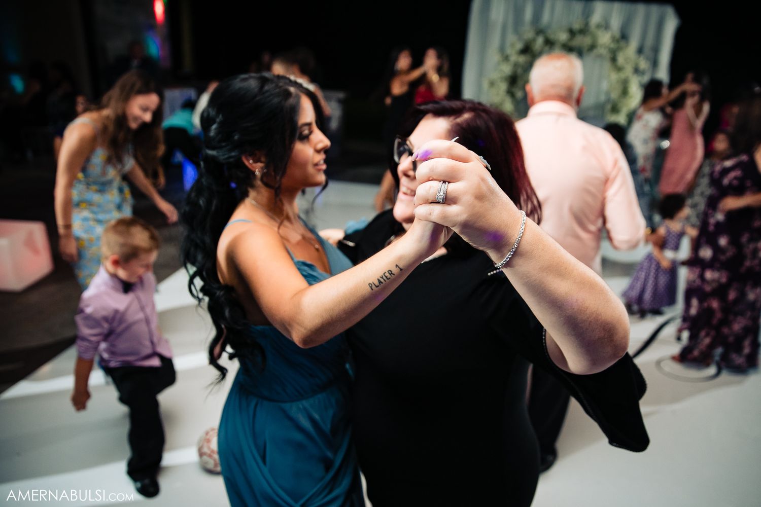 Guests dancing together on reception dance floor with colorful lighting.