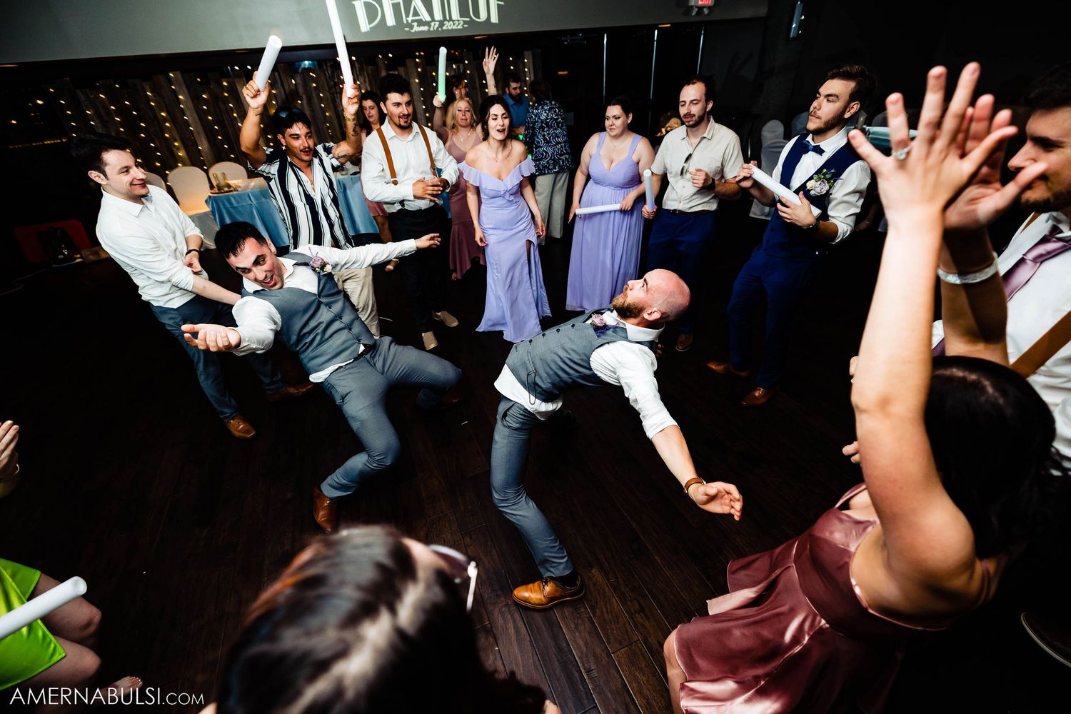 Wedding party members performing dramatic dance moves on dark hardwood floor.