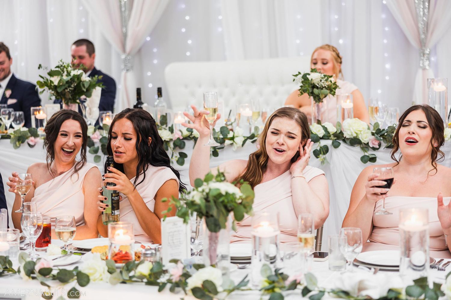 Bridesmaids in pink dresses react joyfully during wedding reception.