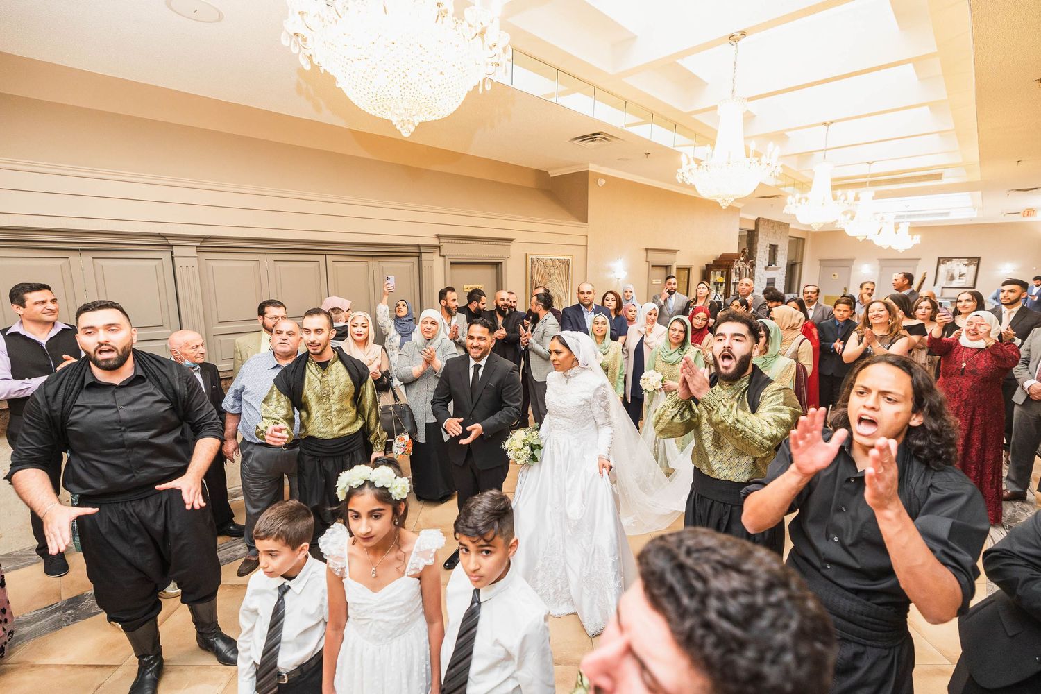 Wedding guests and children celebrating in an elegant ballroom with chandeliers.