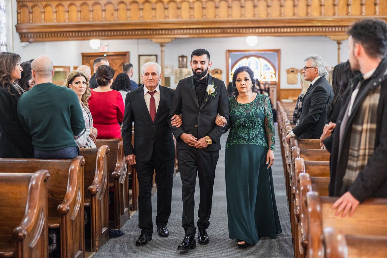 Wedding guests stand in church pews as attendants walk down the center aisle.
