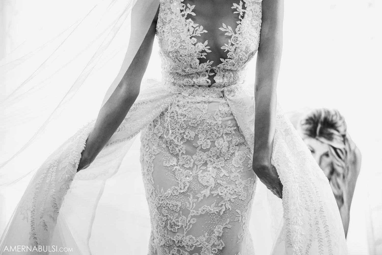 Silhouette of bride in lace dress against sunlit window with flowing veil.