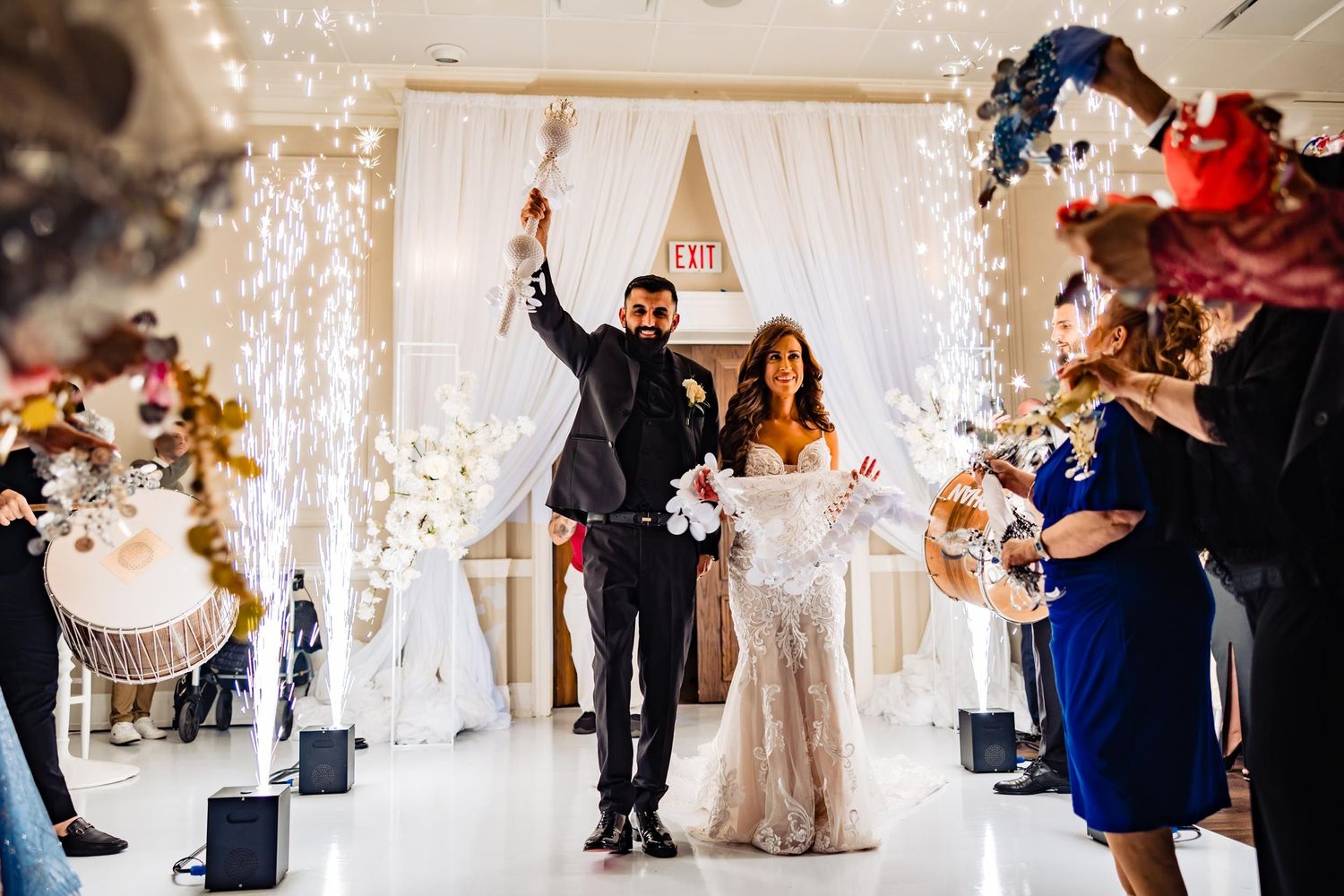 Newlyweds celebrate their entrance under white drapery and sparkling fountains.