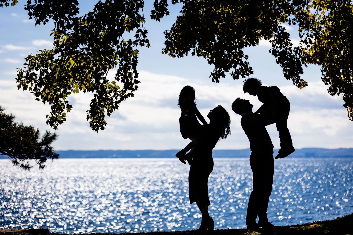 Silhouette of a family playing with children against a sparkling waterfront backdrop.