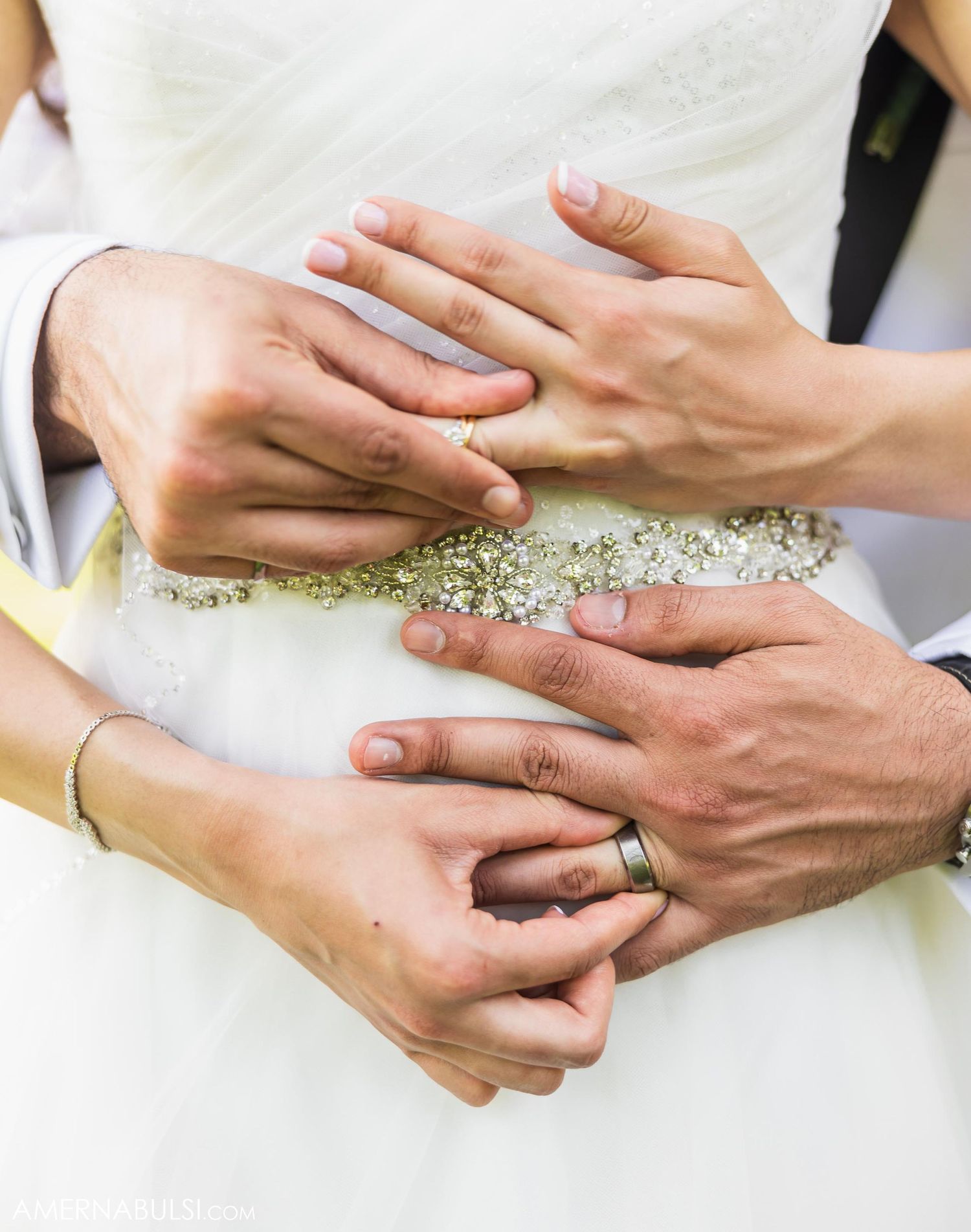 Close-up of hands displaying wedding rings and intricate dress details.