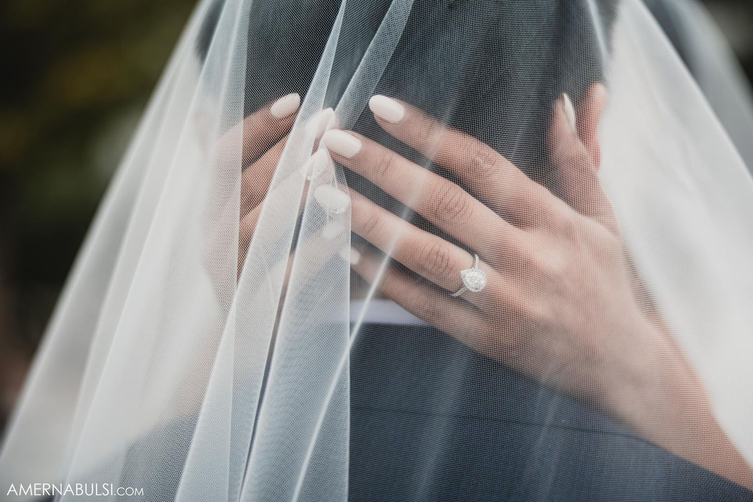 Close up shot of bride's hand with wedding ring through delicate white veil.