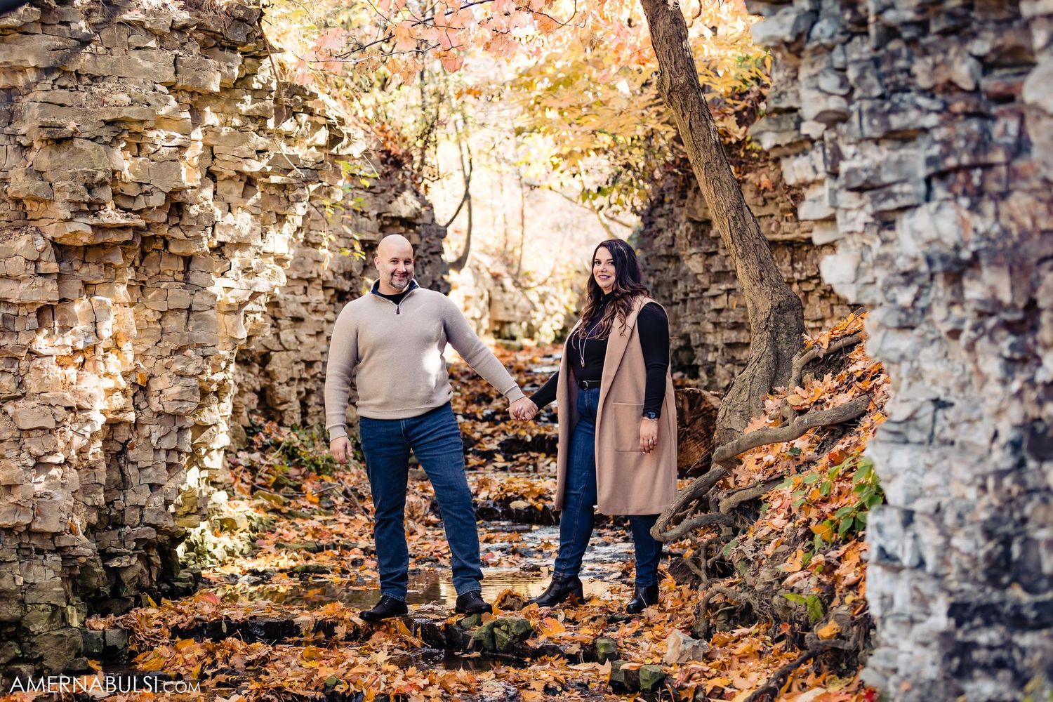 Couple standing together in autumn ruins surrounded by colorful fall foliage and stone walls.