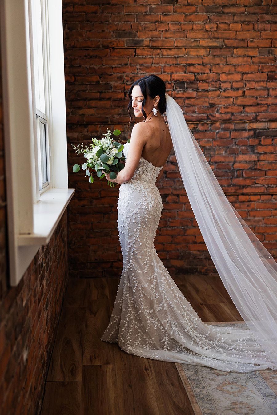 A stunning bridal portrait series against exposed brick walls showcasing an elegant beaded wedding gown with flowing veil.