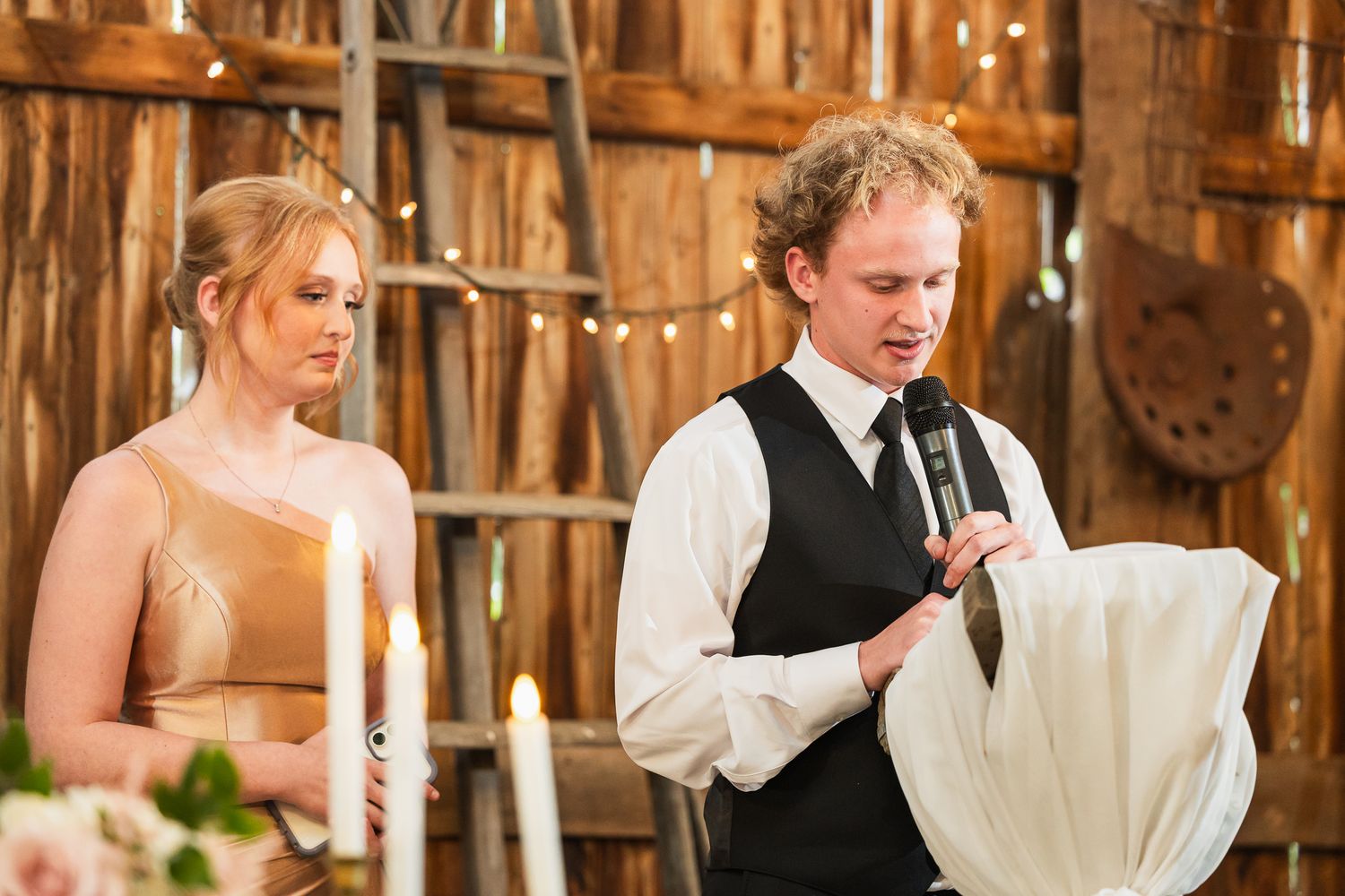 Inside a rustic wooden barn, wedding reception tables are set with elegant white decor and candles.