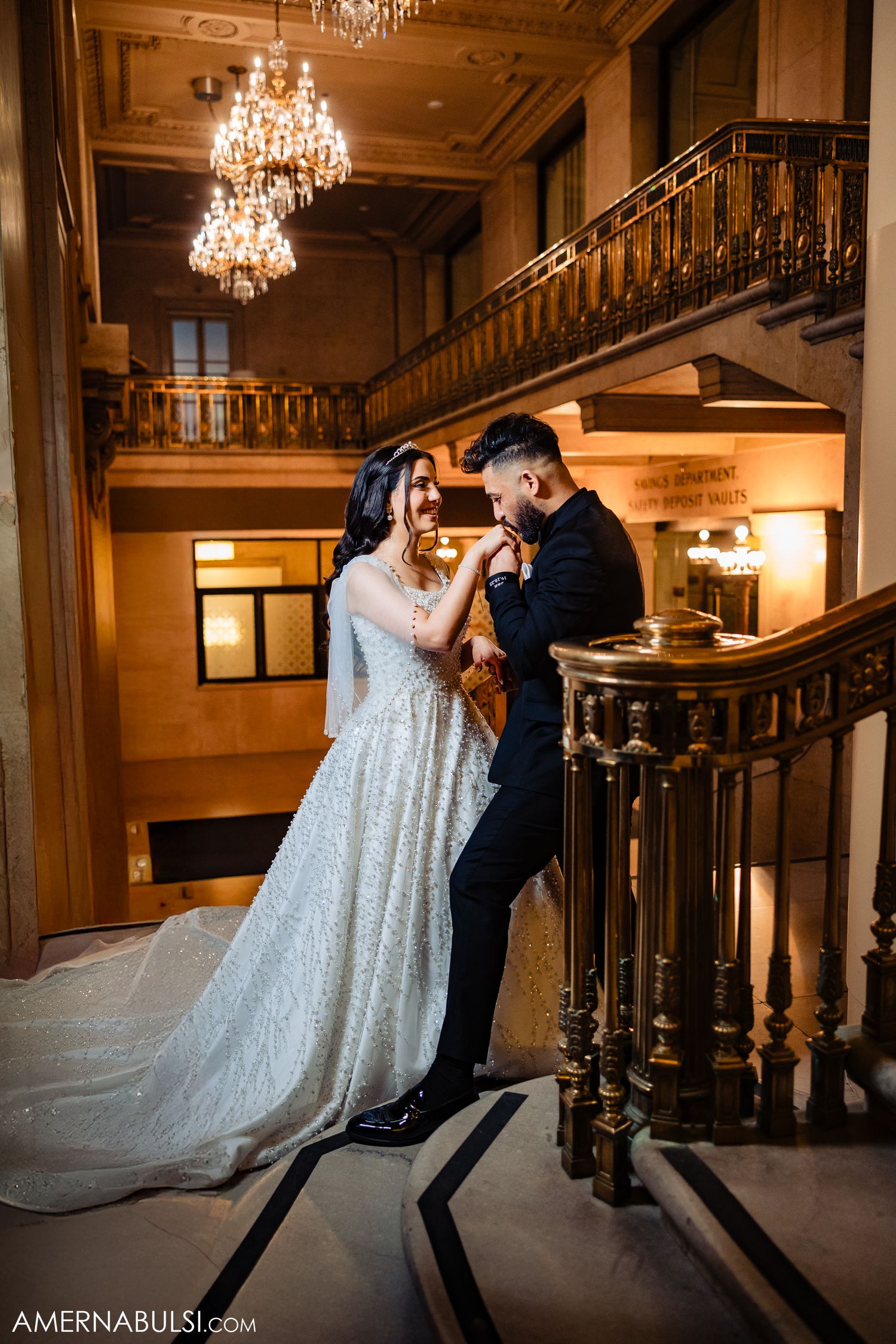 A romantic moment captured on an ornate staircase with crystal chandeliers in an elegant venue.