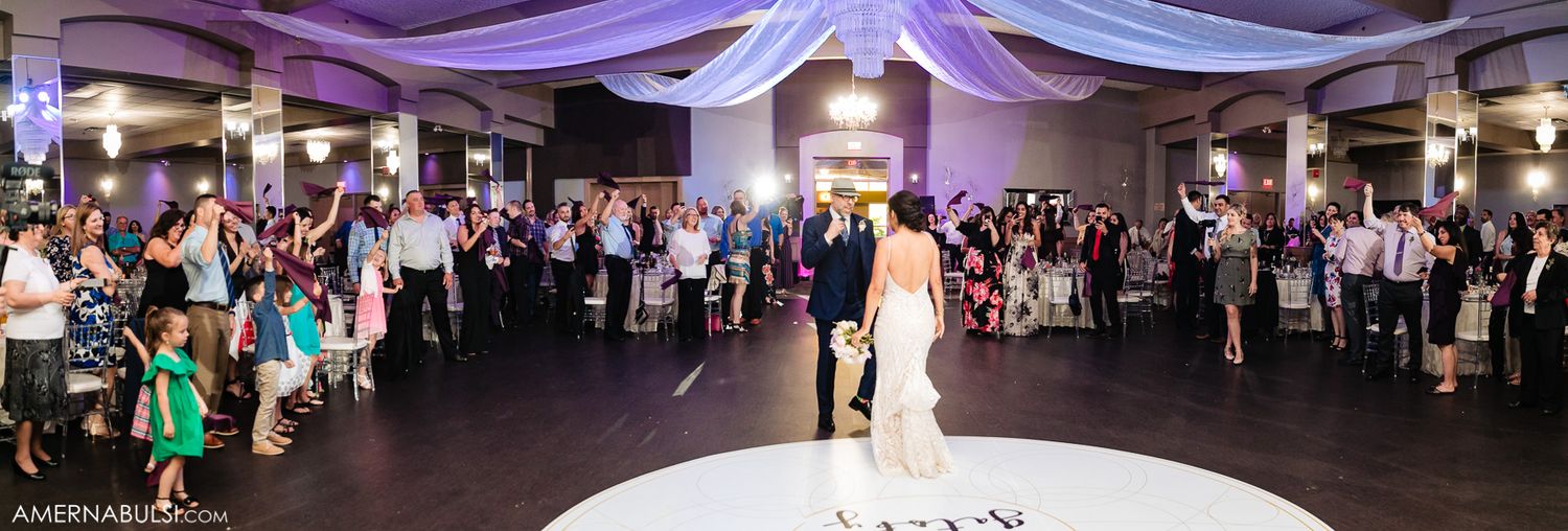 Panoramic view of an elegant wedding venue with white draping, uplighting and a packed dance floor.