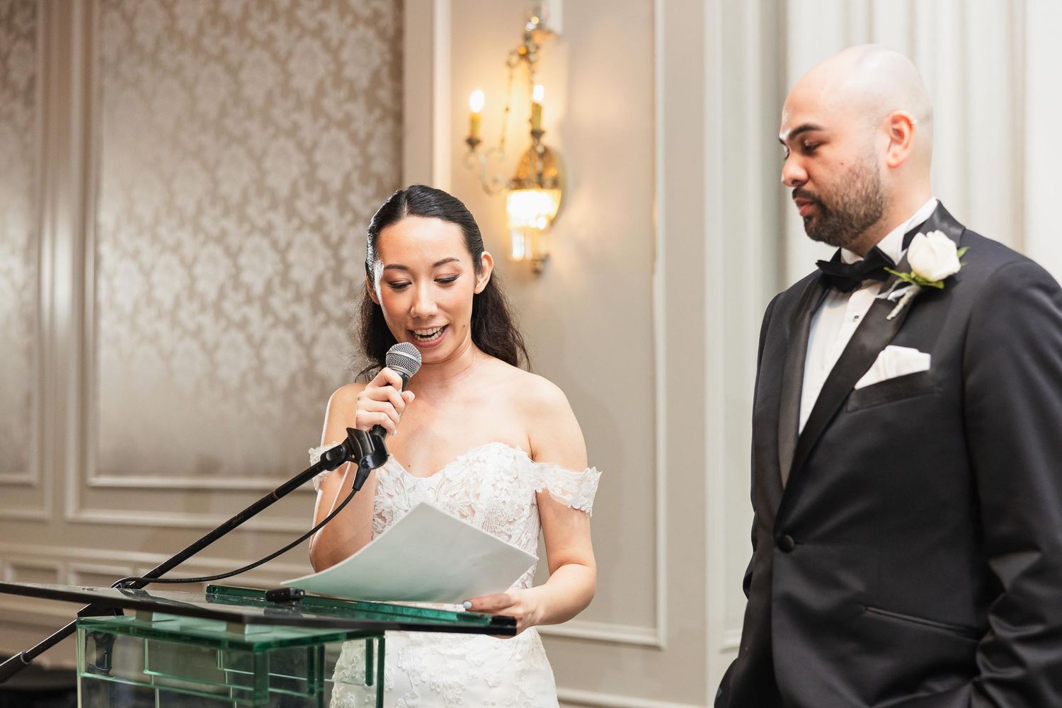 Bride speaks at glass podium during wedding reception speech.