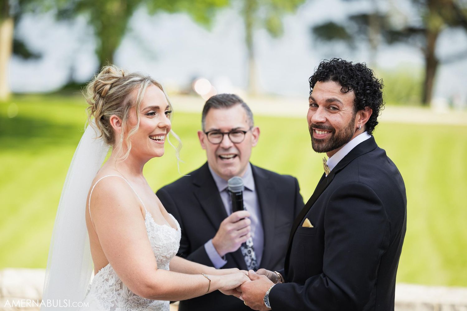 A wedding ceremony taking place outdoors with a couple exchanging vows in front of an officiant on a sunny day.