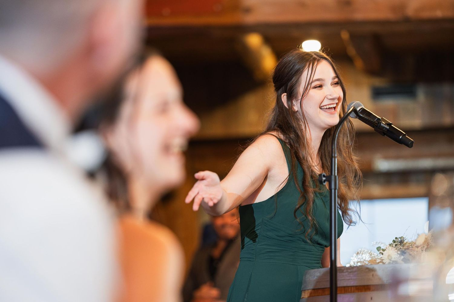 A woman in a dark green dress sings passionately into a microphone at a reception.