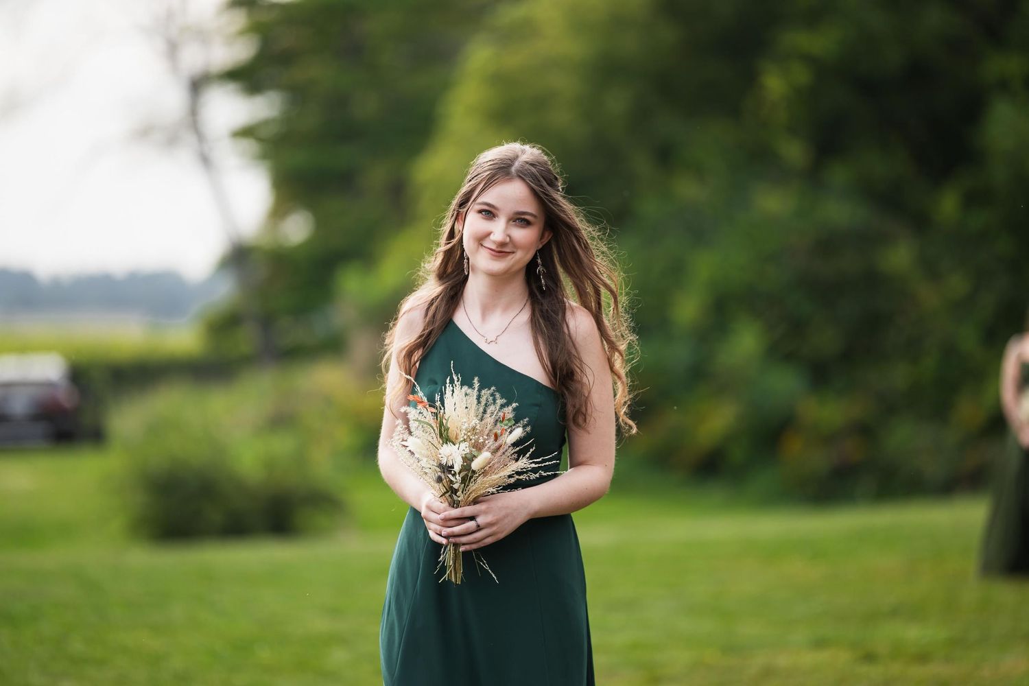 Bridesmaid in green dress holds dried flower bouquet during outdoor ceremony.