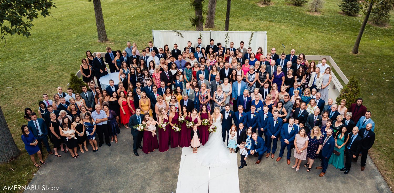 Large wedding party group photo taken outdoors on a lush green lawn.