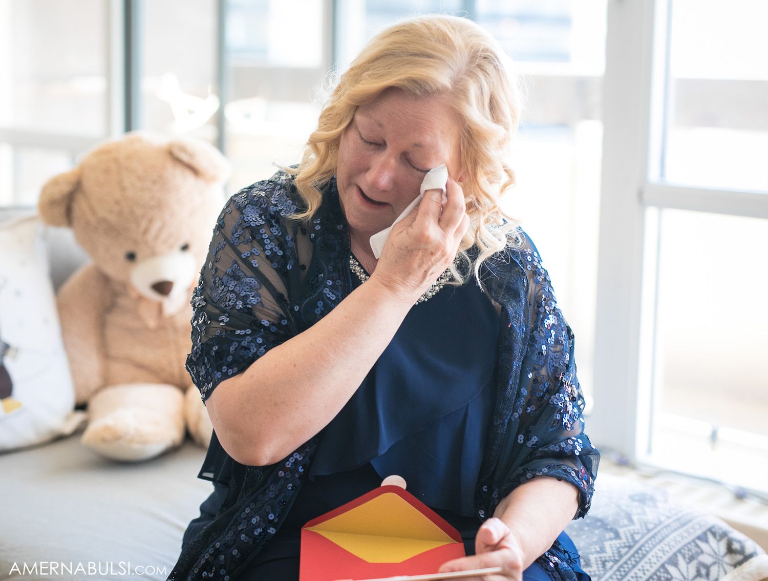 Emotional moment during gift opening with teddy bear visible in background.