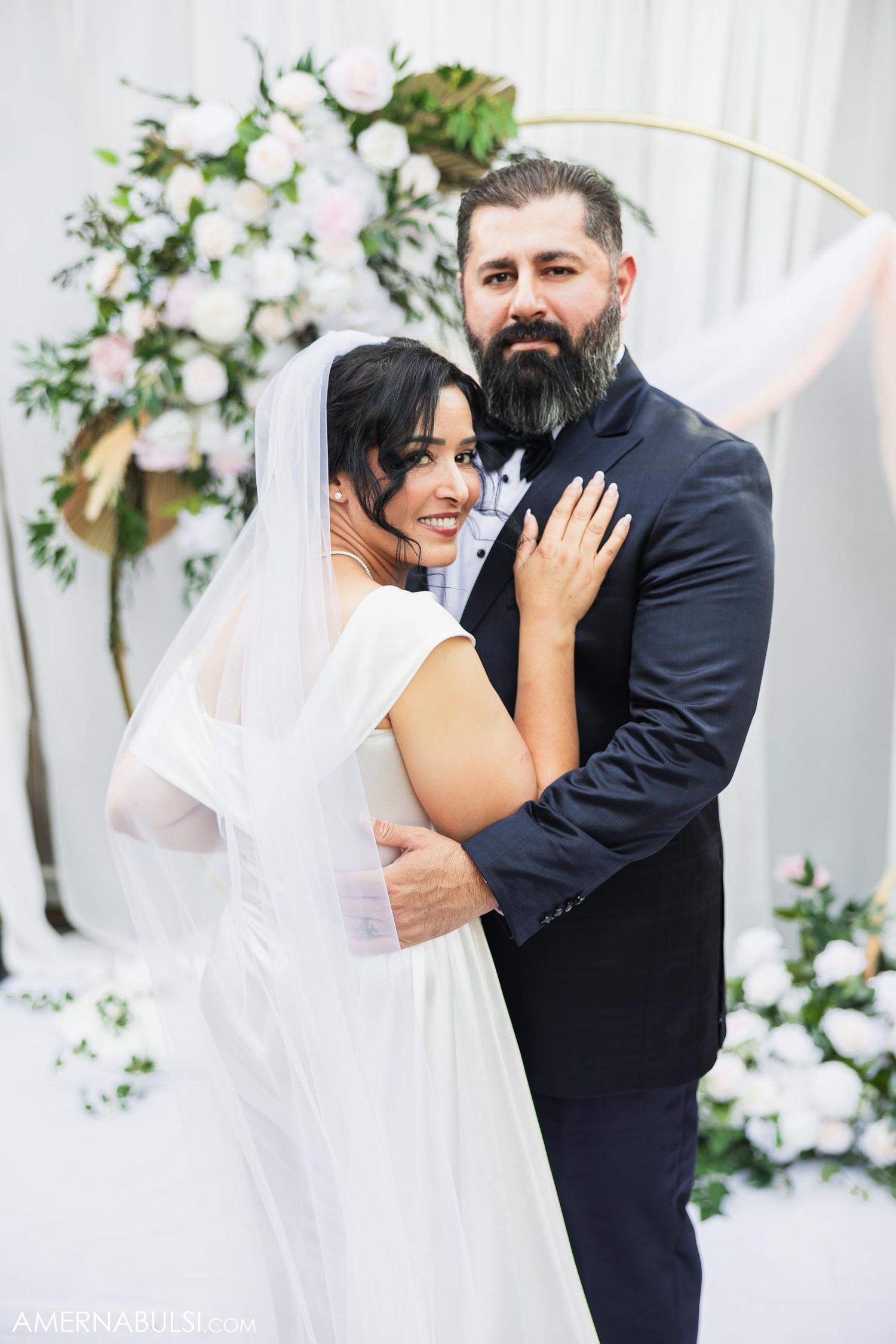 Tender moment between couple in wedding attire against floral backdrop.