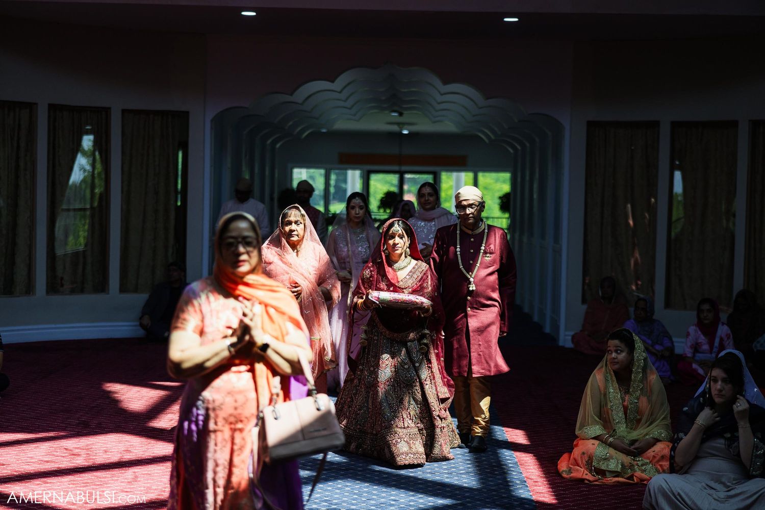 Wedding party members in traditional Indian attire walking through an indoor venue.