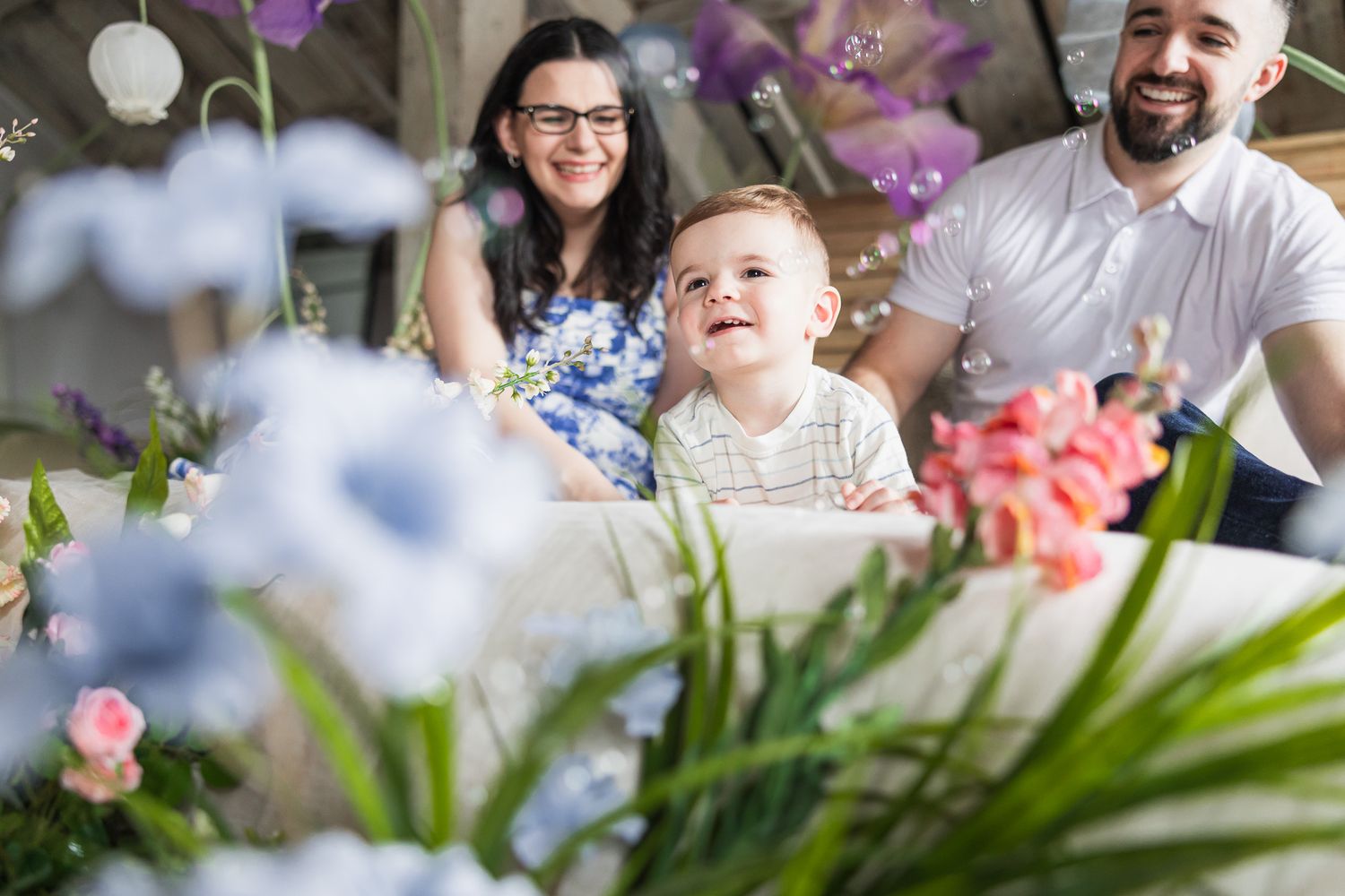 A joyful family moment captured among purple and white flowers in a bright studio setting.