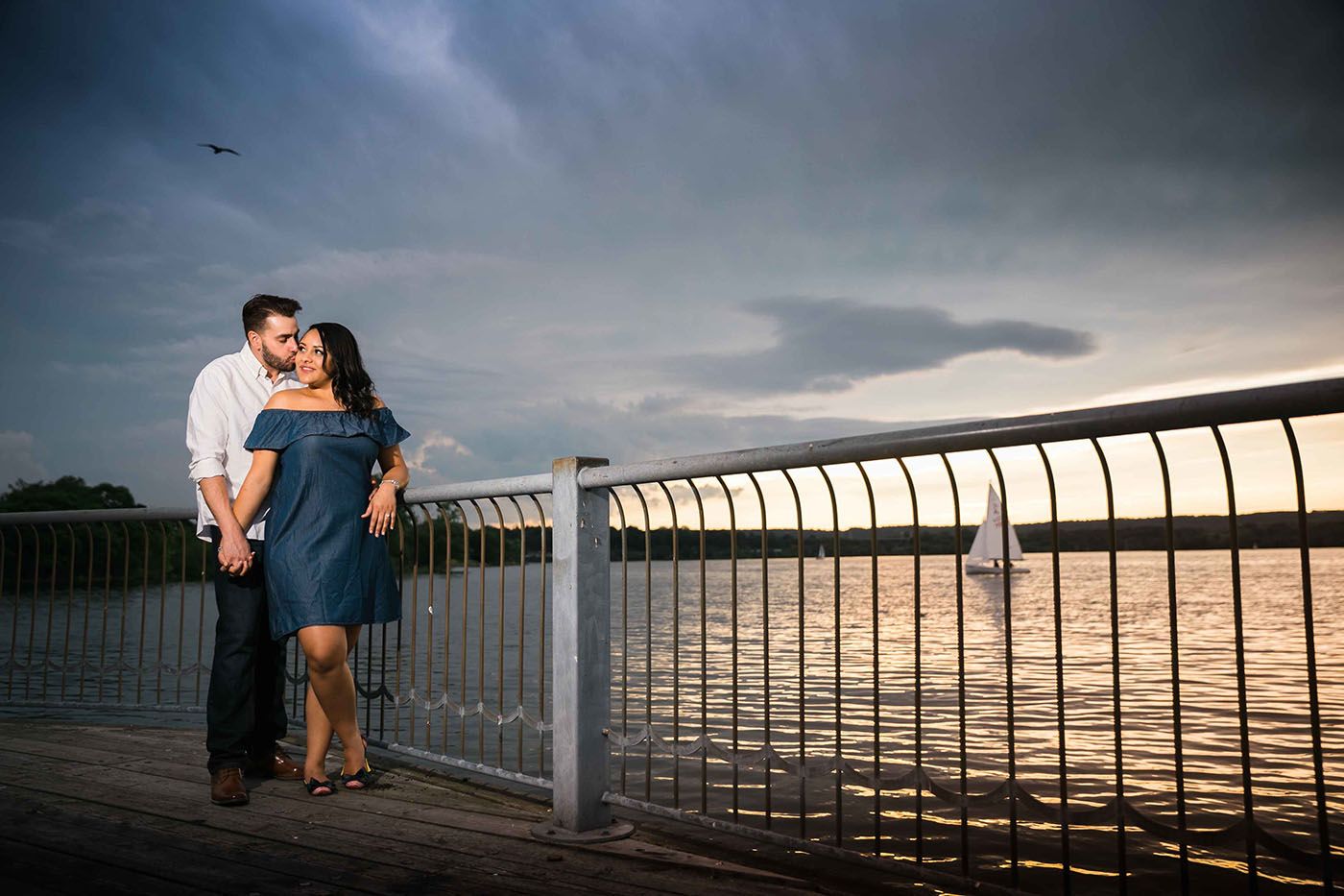 A couple embraces on a pier during a dramatic cloudy sunset.