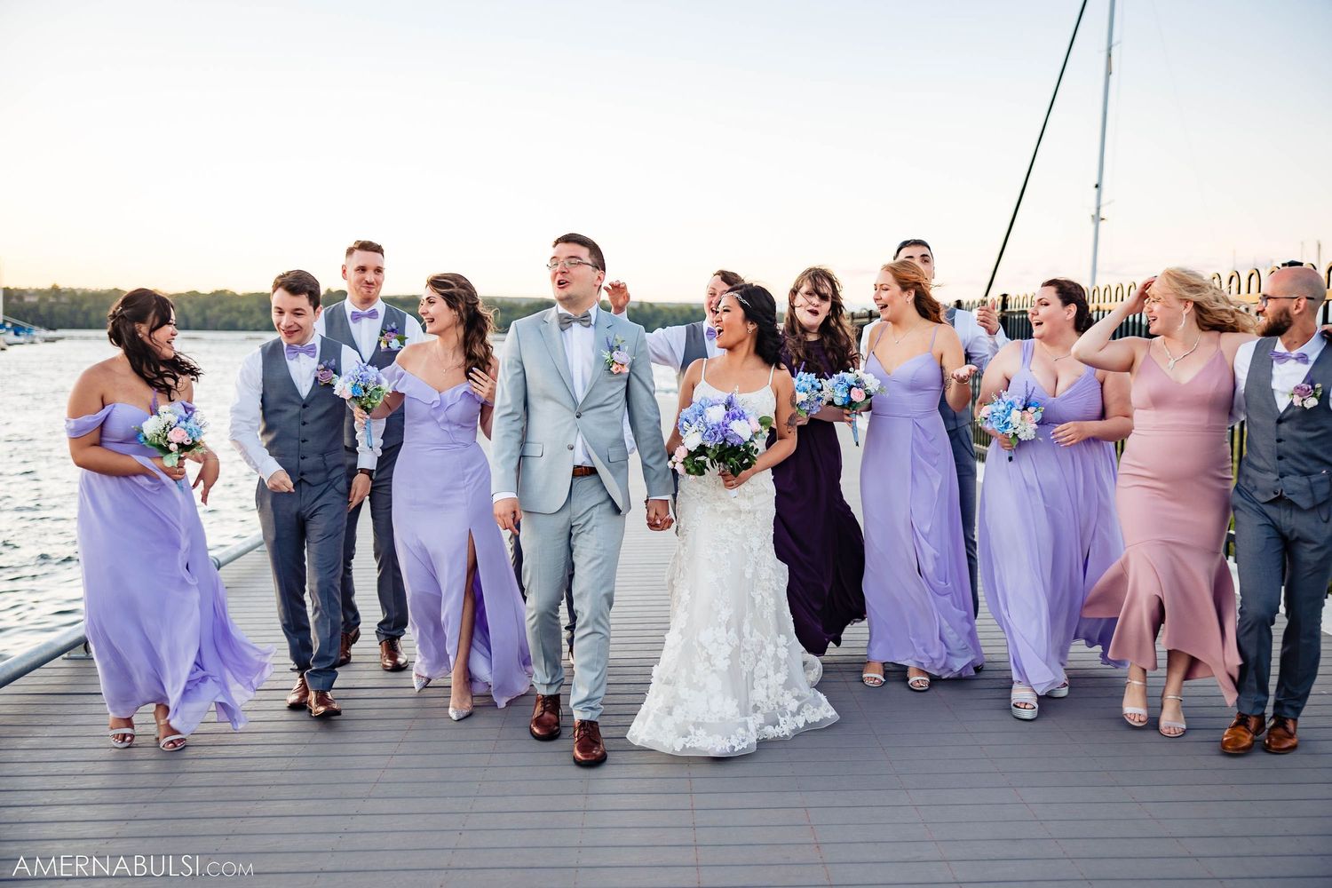Wedding party walking together on dock wearing coordinated purple and gray attire.