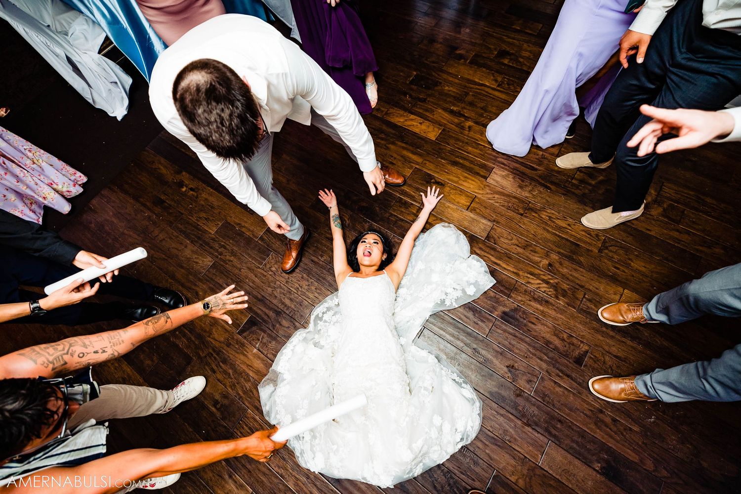 Overhead view of wedding guests dancing around person in white dress on wooden floor.