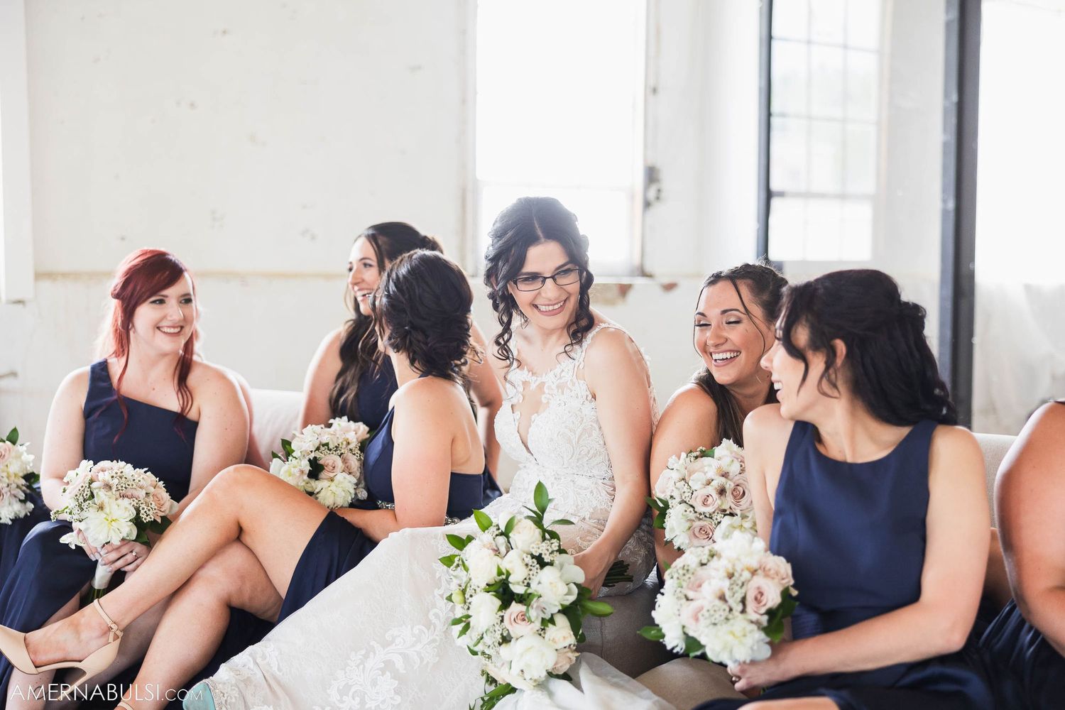 Bridal party shares joyful moment while holding white floral bouquets.