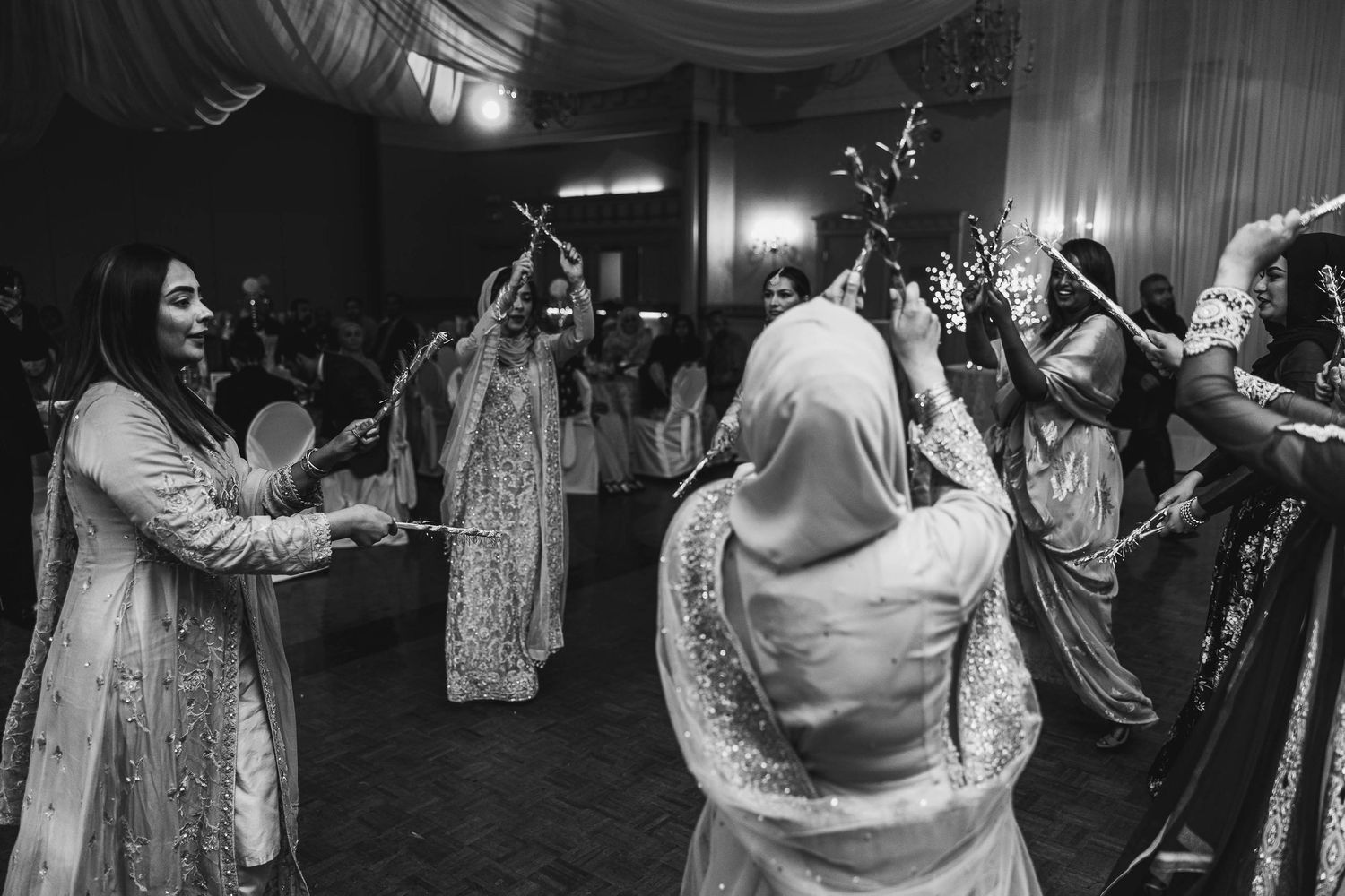 Wedding guests in traditional attire dancing and celebrating on the dance floor in black and white.