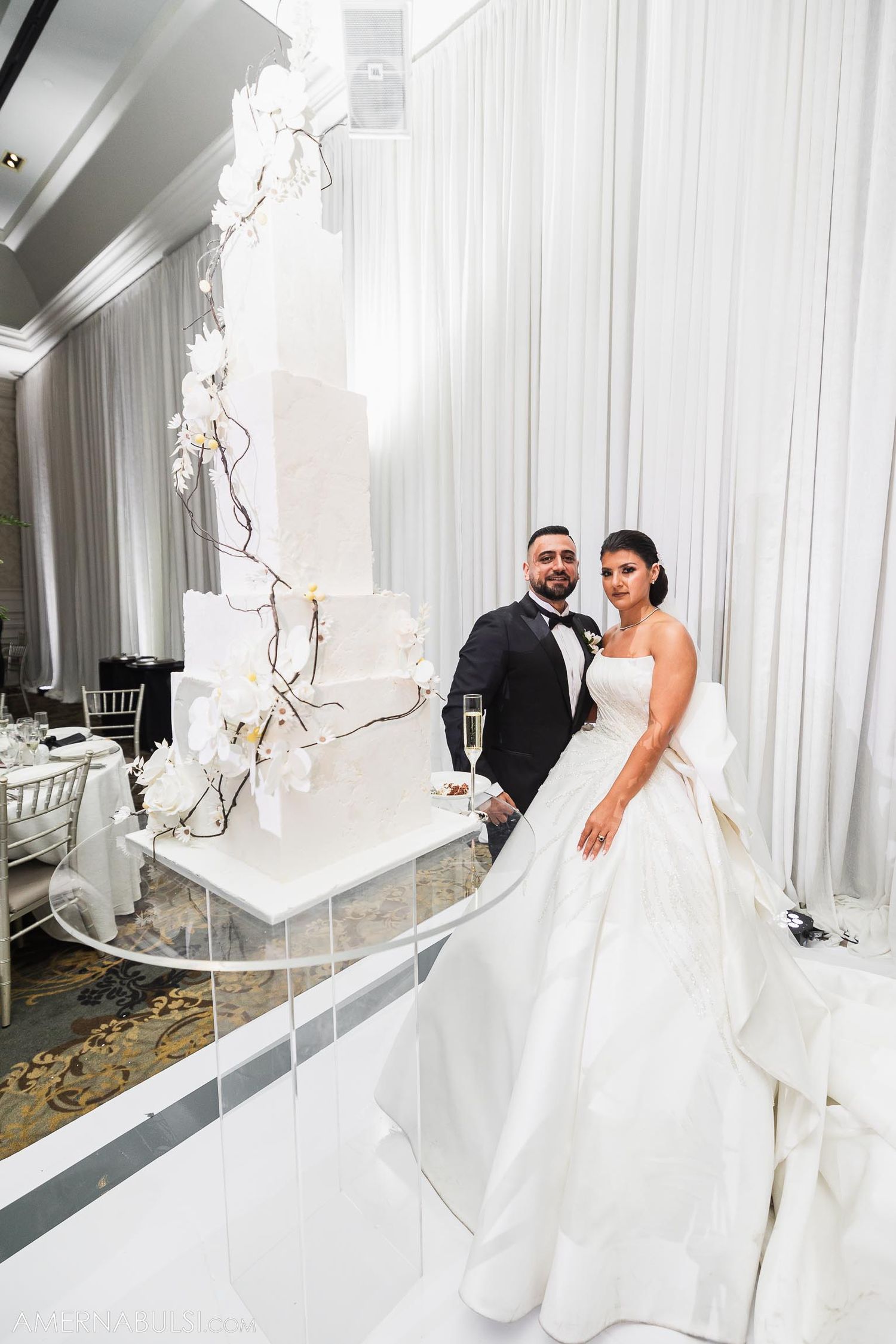 Elegant wedding portrait featuring a stunning white cake display and draped backdrop.