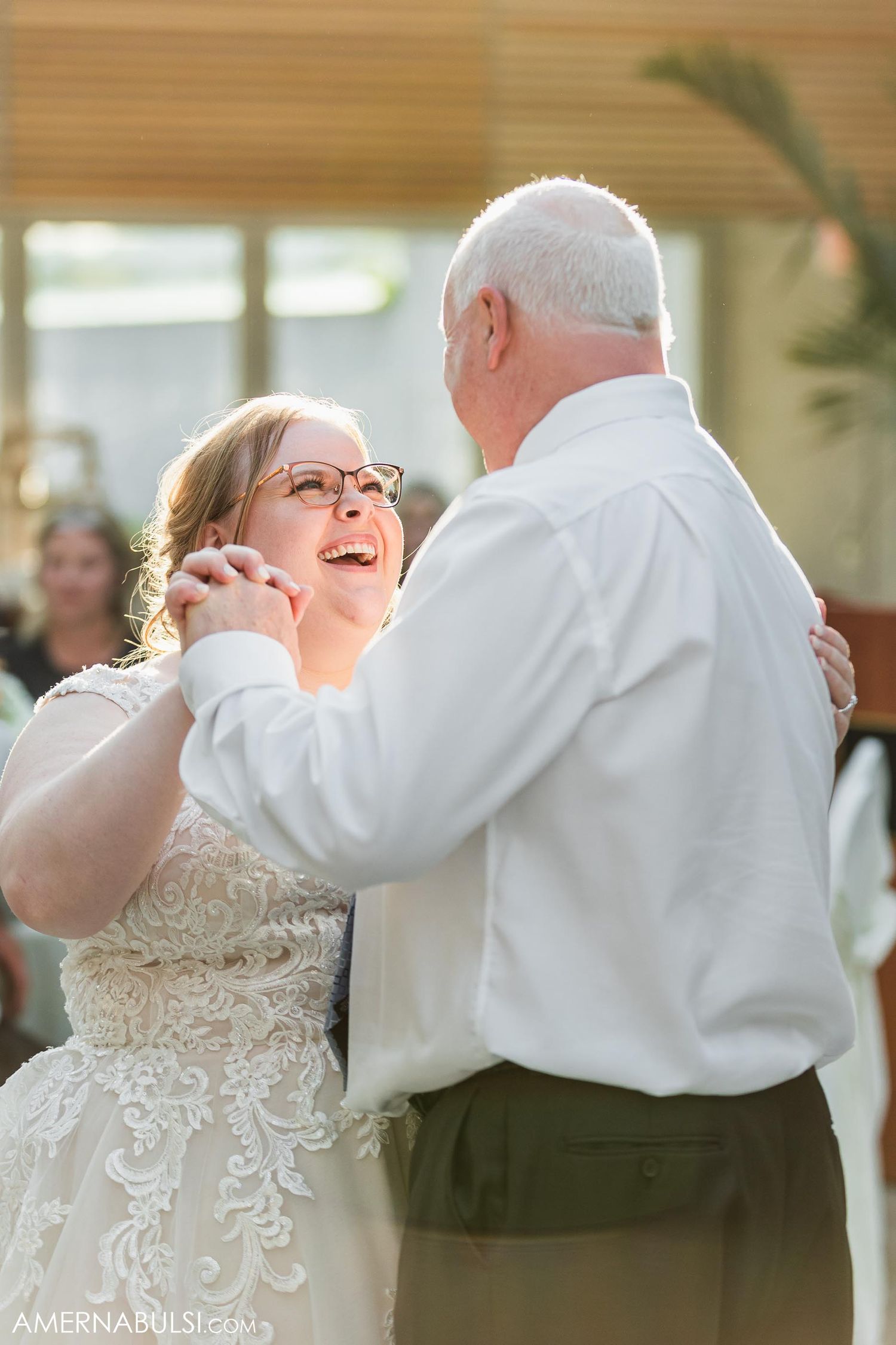 Two people share a laughter-filled dance moment at an indoor wedding reception.