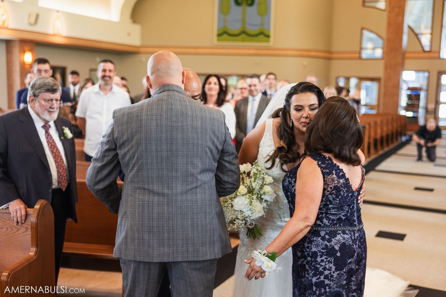 Wedding guests gather inside a church with warm lighting and decorative wall accents.