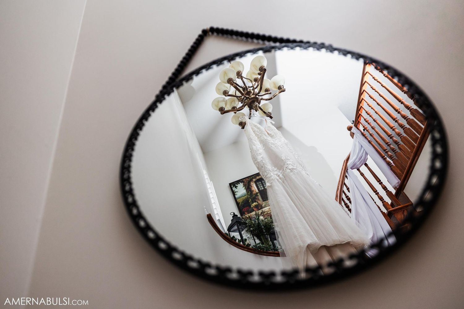Decorative round mirror on wall reflecting chandelier and ceiling details.