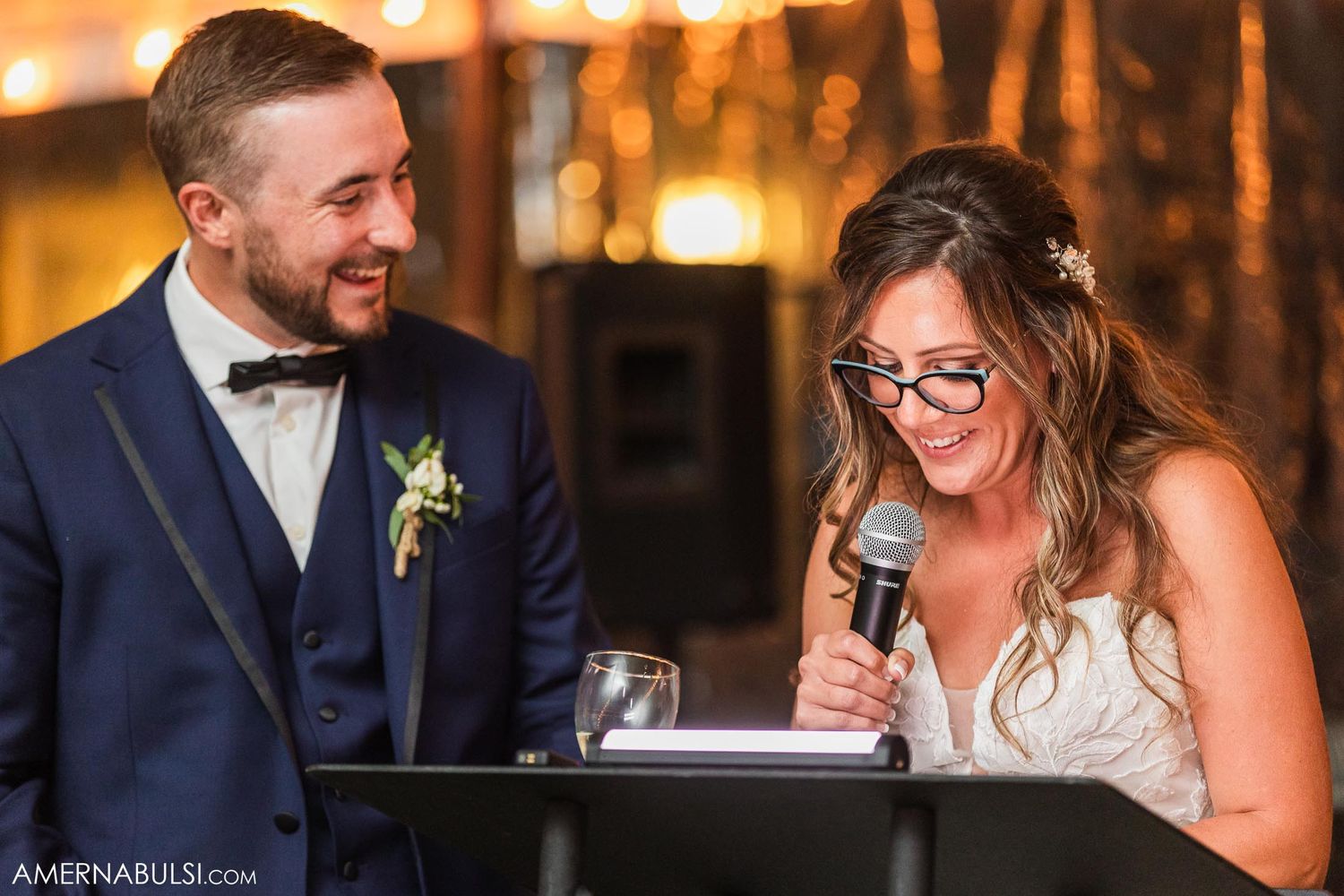 Sweet moment between newlyweds during reception speeches under twinkling lights.
