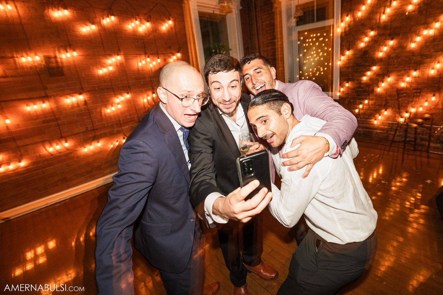 Guests gather close together to take a selfie at an event with warm lighting in the background.