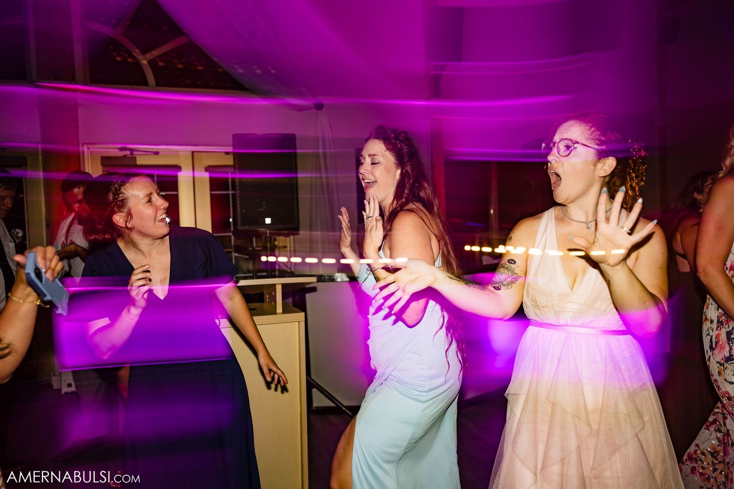People dancing and socializing at a party with purple lighting and entertainment in the background.