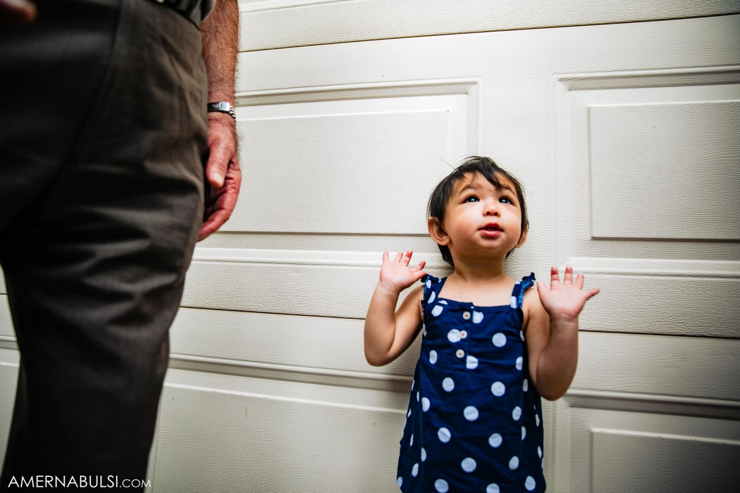 Small child in polka dot dress plays and gestures against white garage door background.