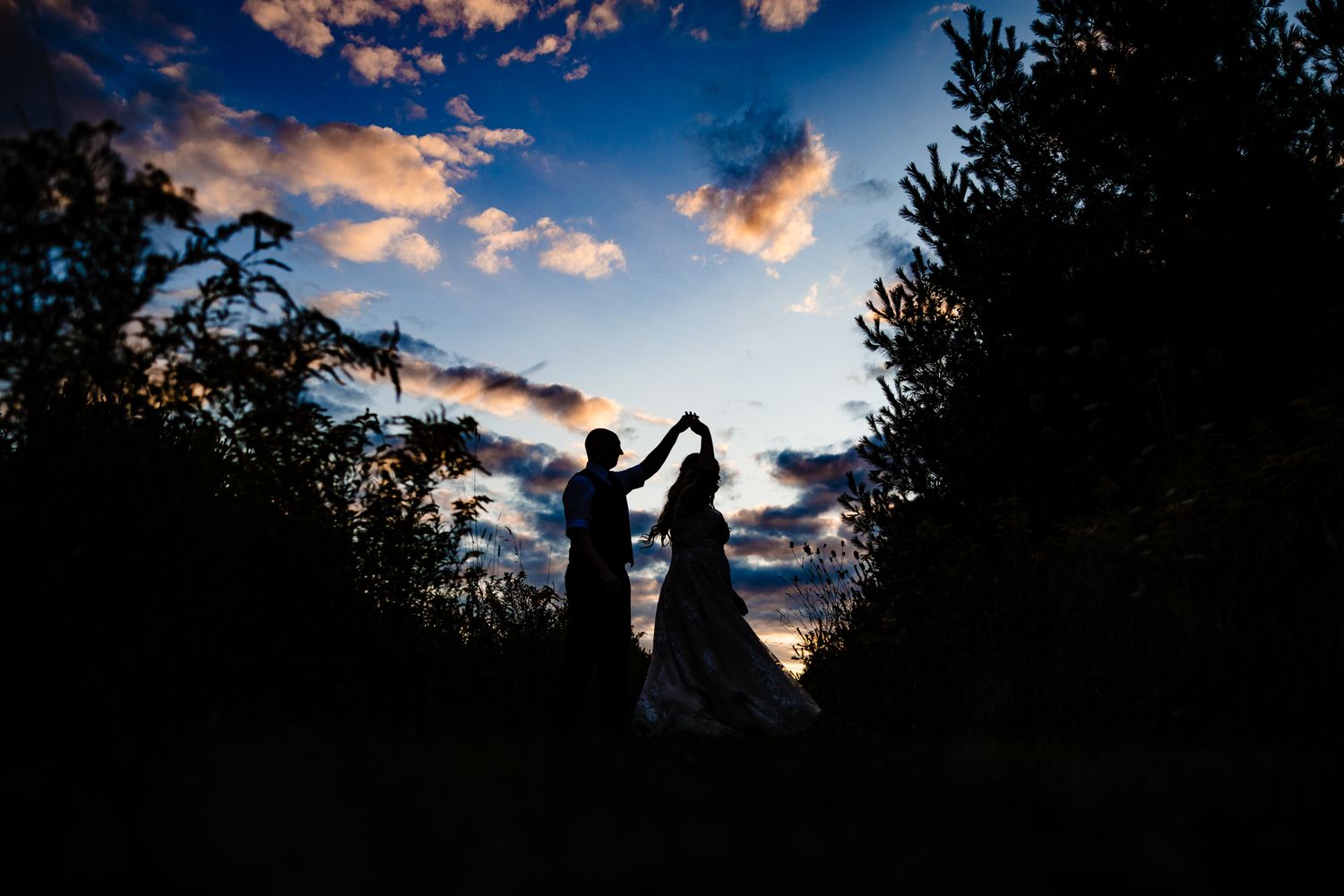 Silhouetted couple poses against a dramatic sunset sky with vibrant orange and blue clouds.