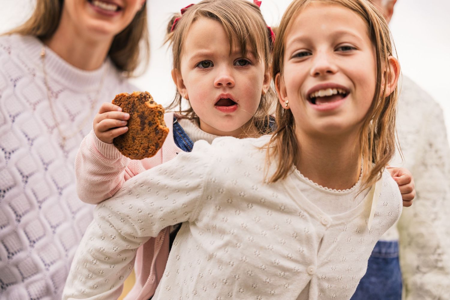 Two children in white sweaters sharing a chocolate cookie with excited expressions.