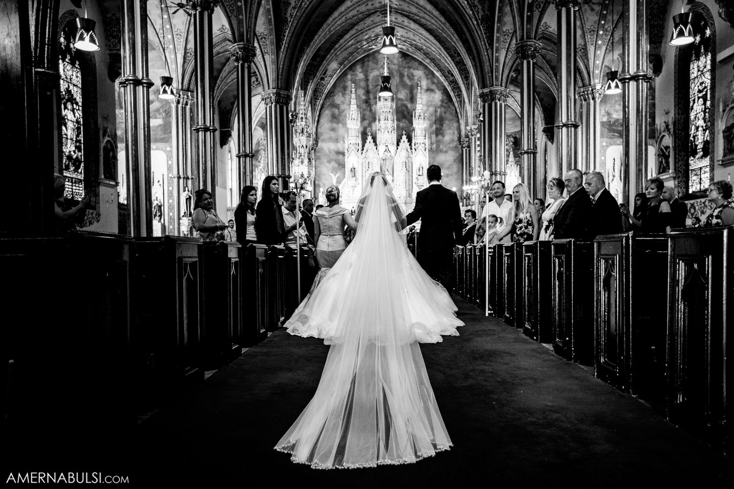 Dramatic black and white photo of a bride in cathedral with gothic arches and stained glass windows.