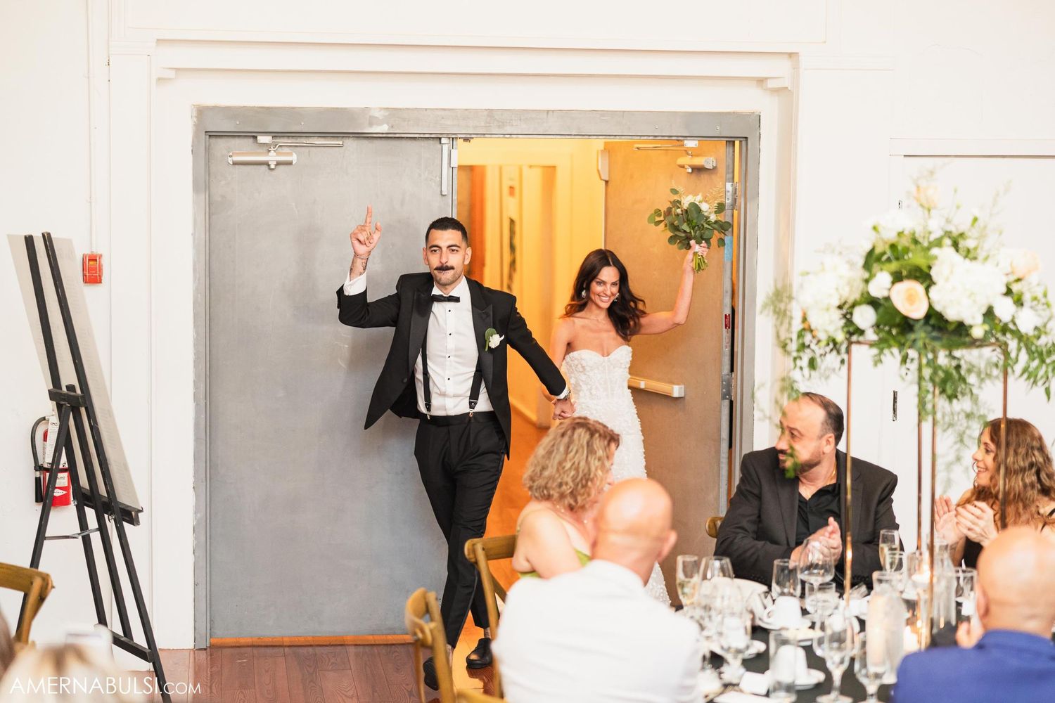 Wedding couple makes grand entrance into reception hall with energetic poses.