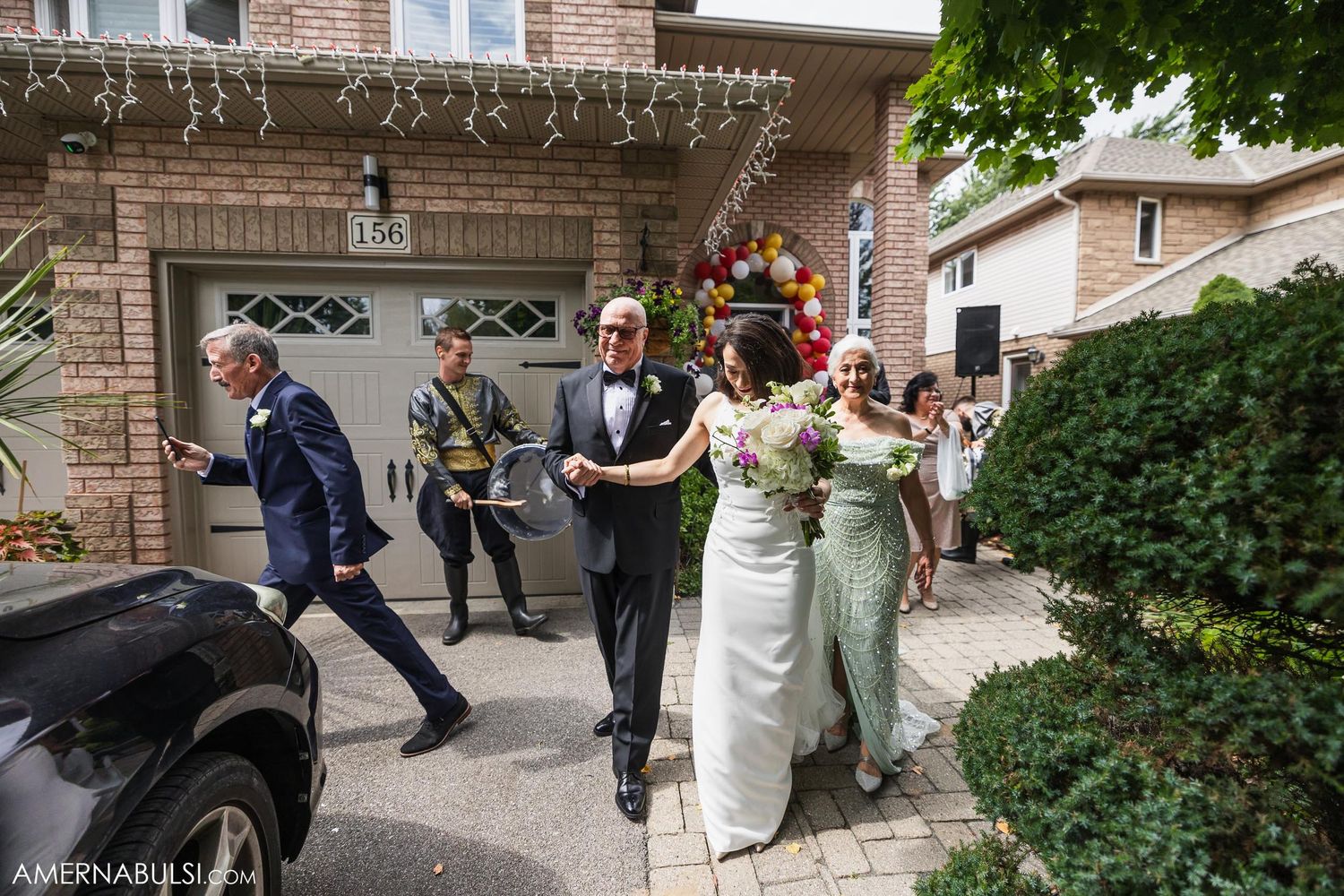 Wedding party walking together outside brick home during celebration.
