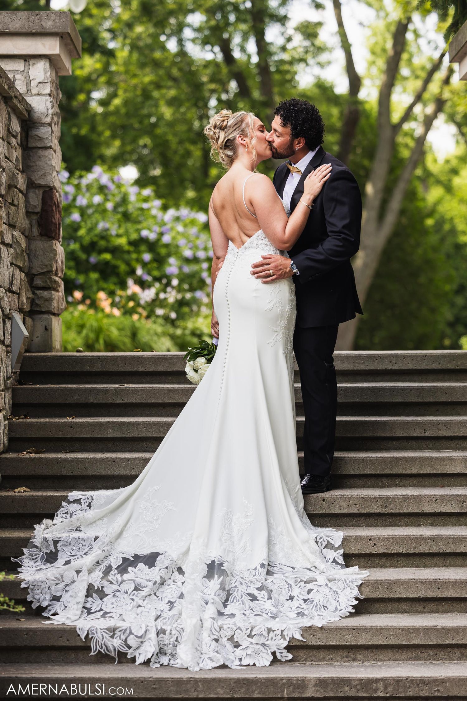A couple shares romantic moment on stone staircase, bride wearing stunning lace-trimmed wedding gown.