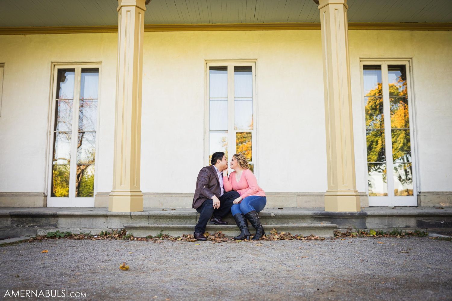 A couple shares an intimate moment while sitting on the steps of a classical building with columns.