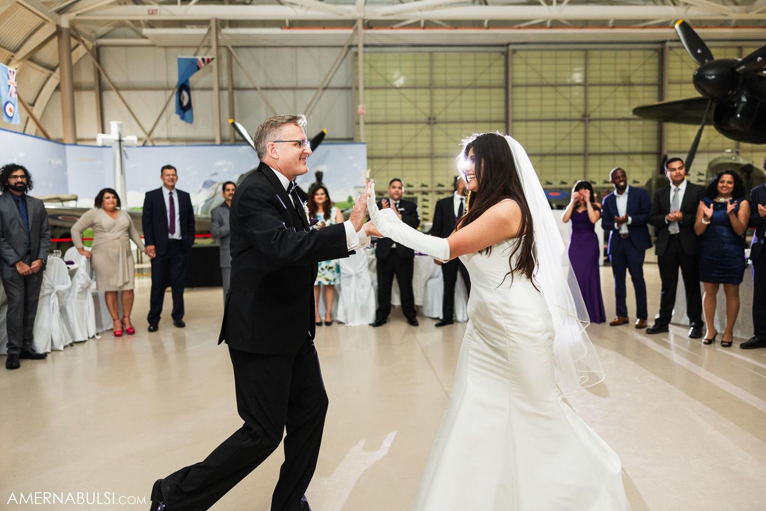 Couple performs energetic dance moves during their first dance in an aviation hangar.