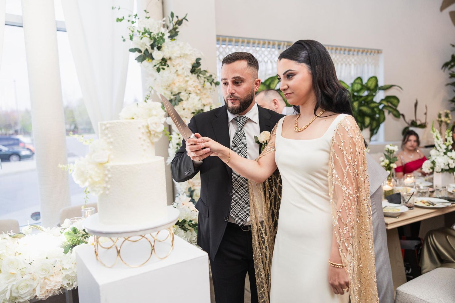 Newlyweds cut their elegant white wedding cake together at the reception.