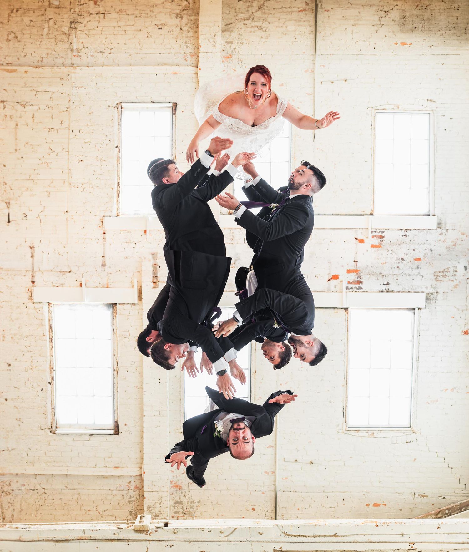Groomsmen performing an acrobatic jump pose with the groom in an industrial indoor setting.