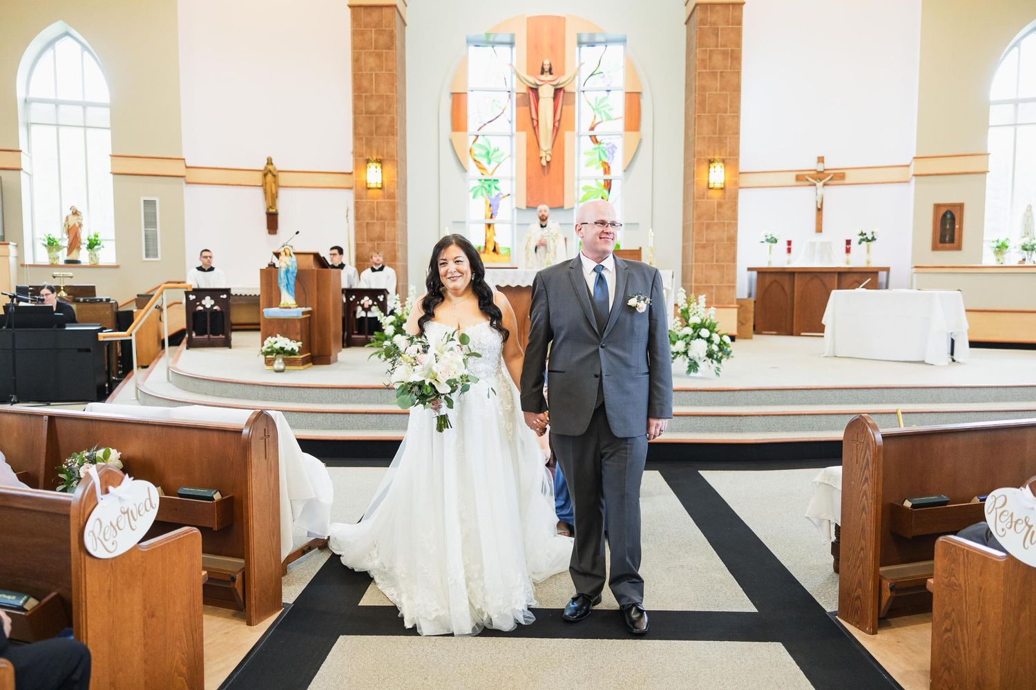 Couple stands at altar in traditional church with wooden pews and stained glass windows.